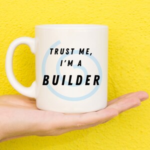 May include: White ceramic mug with a blue swirl design and the text "TRUST ME, I'M A BUILDER".