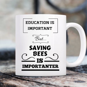 May include: White ceramic coffee mug with black text that reads "Education is important, but... Saving Bees is importanter."
