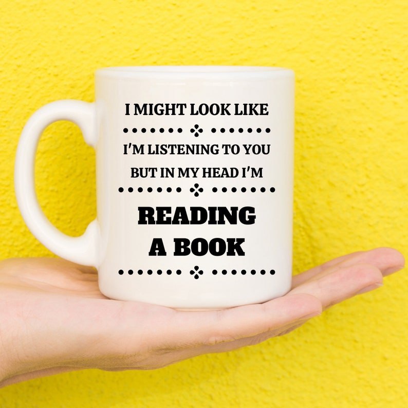 May include: White ceramic mug with black text that reads "I might look like I'm listening to you but in my head I'm reading a book".