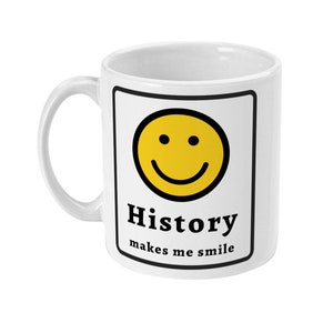 K&ouml;nnte beinhalten: Wei&szlig;e Keramiktasse mit schwarzem Rand und einem gelben Smiley. Der Text "History makes me smile" ist auf die Tasse gedruckt.