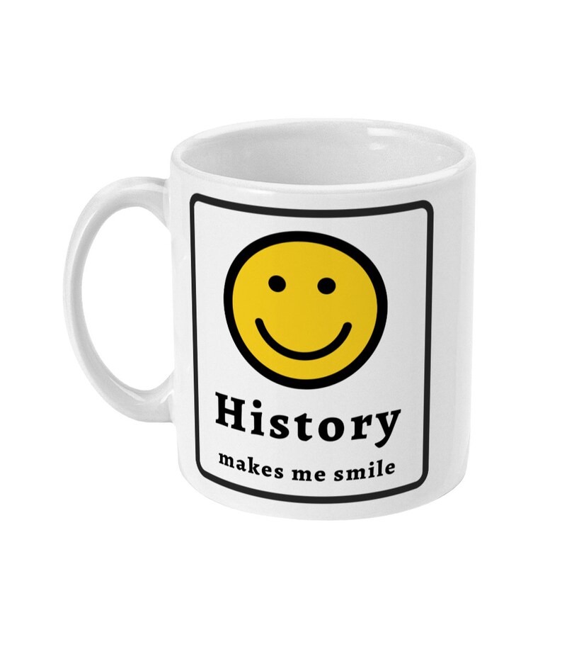 K&ouml;nnte beinhalten: Wei&szlig;e Keramiktasse mit schwarzem Rand und einem gelben Smiley. Der Text "History makes me smile" ist auf die Tasse gedruckt.