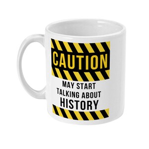 K&ouml;nnte beinhalten: Wei&szlig;e Keramiktasse mit einem schwarzen und gelben Warnschild mit der Aufschrift "ACHTUNG KANN ANFANGEN &Uuml;BER GESCHICHTE ZU REDEN".