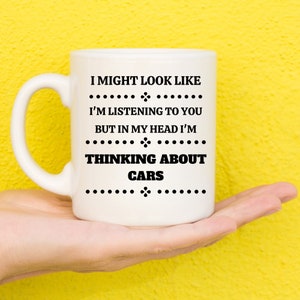 May include: White ceramic coffee mug with black text that reads "I might look like I'm listening to you but in my head I'm thinking about cars".