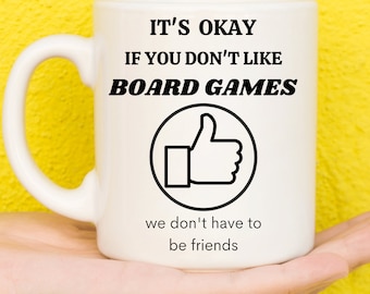 May include: White ceramic mug with black text that reads "It's okay if you don't like board games. We don't have to be friends." A black thumbs up icon is in a circle.