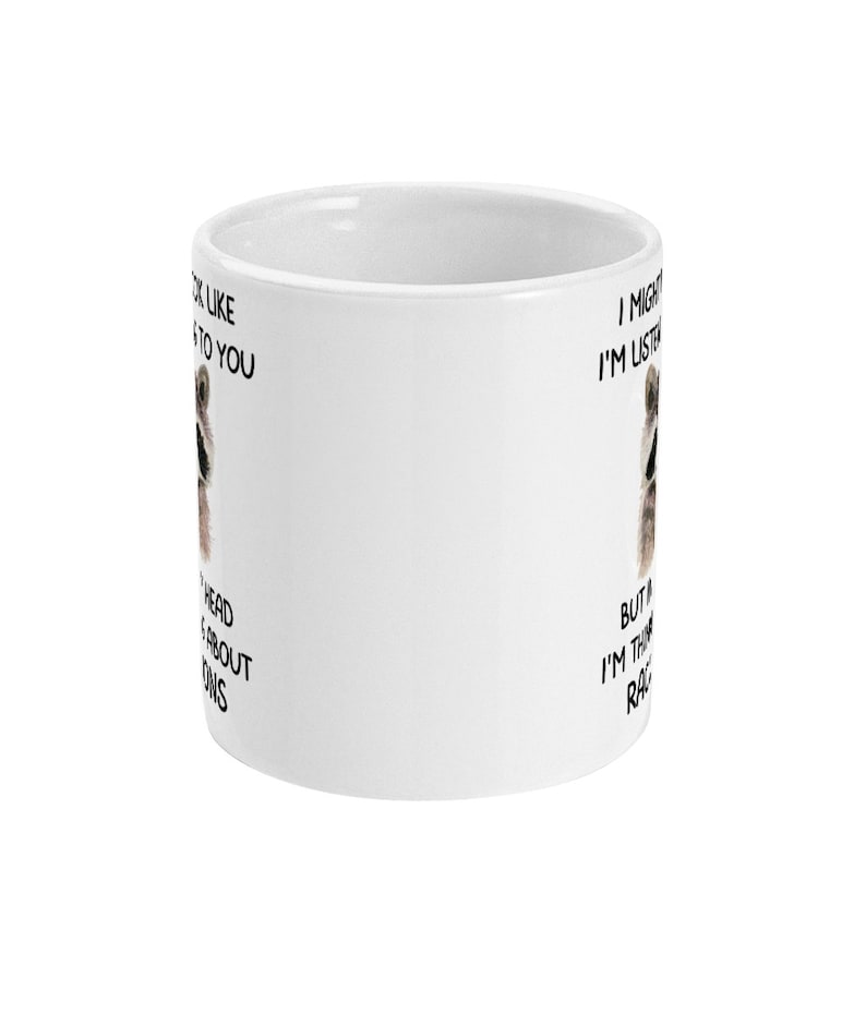 May include: White ceramic mug with a raccoon face and the text "I might look like I'm listening but actually I'm thinking about raccoons".