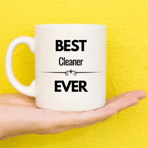 Peut inclure: Une tasse en céramique blanche avec du texte noir qui dit "BEST Cleaner EVER".