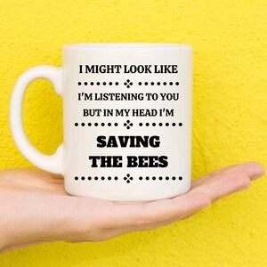 May include: White ceramic mug with black text that reads "I might look like I'm listening to you but in my head I'm saving the bees".