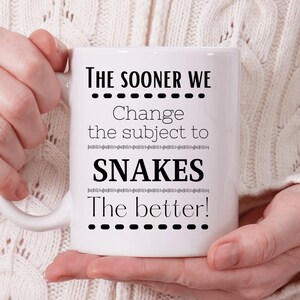 Op de afbeelding: Een witte keramische koffiemok met zwarte tekst die "The sooner we change the subject to snakes the better!" luidt.