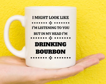 Könnte beinhalten: Weiße Keramiktasse mit schwarzem Text, der lautet: "Ich sehe vielleicht so aus, als würde ich zuhören, aber in meinem Kopf trinke ich Bourbon".