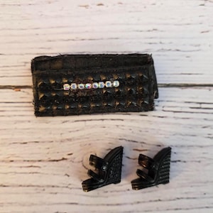 May include: Black miniature handbag with a studded texture and a row of iridescent rhinestones. Two black wedge sandals with multiple straps are also present, suggesting a fashion accessory set.
