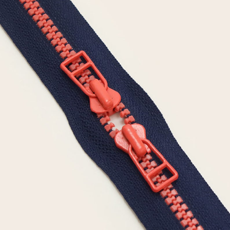 May include: A close-up of a navy blue zipper with pink plastic teeth. The zipper is open and the slider is visible.