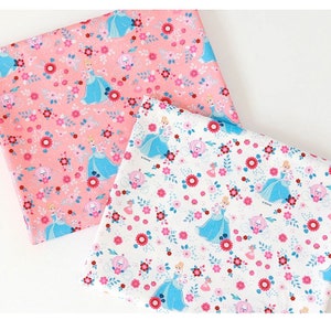 May include: Two fabric panels with a repeating pattern of Cinderella in a blue dress, a carriage, and pink and white flowers. One panel is pink and the other is white.