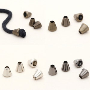 May include: Assortment of metal cord end tips in three colors: silver, bronze, and black. The tips are cone-shaped and have a hole in the center for threading cord.