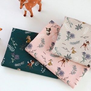 May include: Three fabric swatches with a woodland theme featuring a repeating pattern of deer, rabbits, and floral designs. The swatches are in shades of green, pink, and beige.