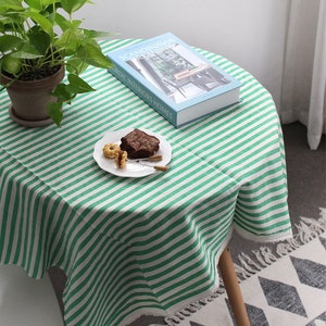 K&ouml;nnte beinhalten: Gr&uuml;n-wei&szlig; gestreifter Tischdecke mit Fransen, ein Buch mit dem Titel "Skandinavien Tr&auml;umen" und ein Teller mit einem Brownie und Keksen auf einem Holztisch.