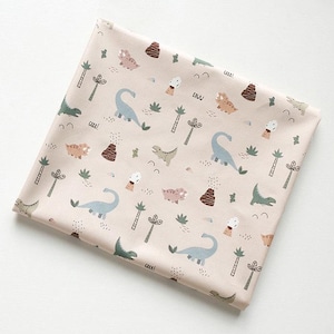 Peut inclure: Un tissu rose pâle avec un motif répété de dinosaures, d'arbres et de volcans. Les dinosaures sont dans des tons de bleu et de vert, et les arbres sont verts. Les volcans sont bruns et orange. Le tissu a une texture subtile.