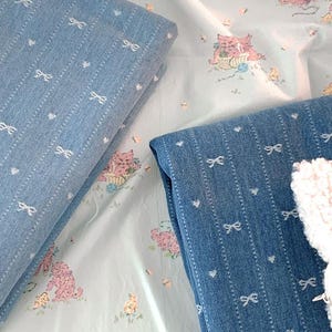 May include: Two pieces of blue denim fabric with white bow patterns. One fabric has a diamond pattern and the other has vertical stripes.