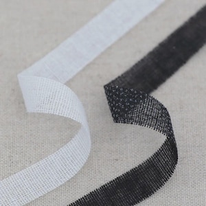 May include: Close-up of two ribbons. One is white, the other black. Both have a woven, mesh-like texture. The ribbons curve gently, creating movement against a neutral background.