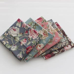Peut inclure: Plusieurs carrés de tissu pliés avec des motifs floraux. Les tissus présentent un motif de grandes roses et de feuilles roses, blanches et vertes sur des fonds gris, bleus et marron. Chaque carré mesure environ 25 cm x 25 cm.