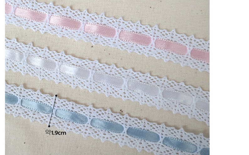 May include: Three white lace trims with different coloured satin ribbon accents. The top trim has pink ribbon, the middle trim has white ribbon, and the bottom trim has light blue ribbon. Each trim is approximately 1.9 cm wide.