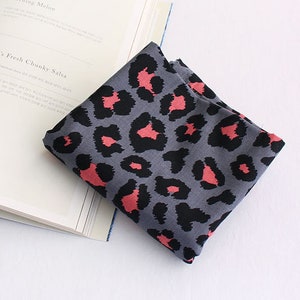 May include: A gray fabric with a pink leopard print pattern. The fabric is folded and lying on a white book.