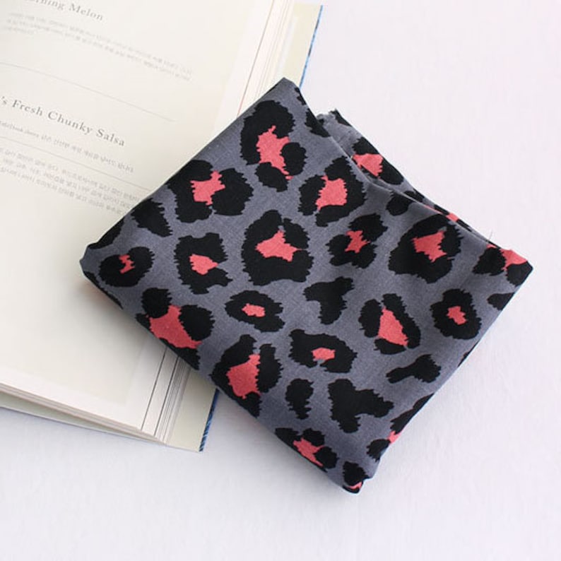 May include: A gray fabric with a pink leopard print pattern. The fabric is folded and lying on a white book.
