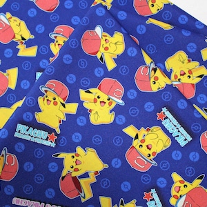 Peut inclure: Tissu bleu avec un motif répété de Pikachu portant une casquette de baseball rouge. Le tissu a une étoile blanche et le texte "Pikachu" dans un encadré rouge.