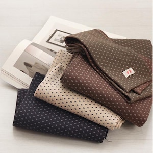 Peut inclure: Plusieurs pochettes pliées de couleurs bleu marine, beige et marron, chacune avec un motif à pois. Une petite étiquette est visible sur l'une des pochettes marron. Les pochettes sont empilées sur un magazine ouvert.