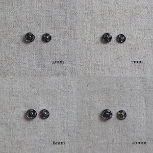 May include: Four pairs of black metal snap fasteners in different sizes: 5mm, 7mm, 8mm, and 10mm. The fasteners are arranged in two rows of two on a beige fabric background.