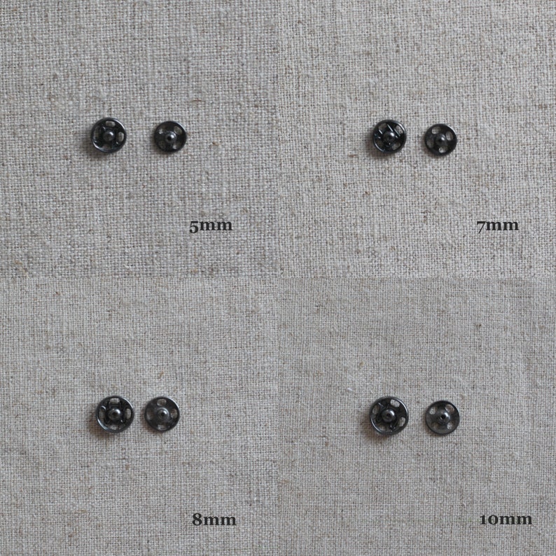 May include: Four pairs of black metal snap fasteners in different sizes: 5mm, 7mm, 8mm, and 10mm. The fasteners are arranged in two rows of two on a beige fabric background.