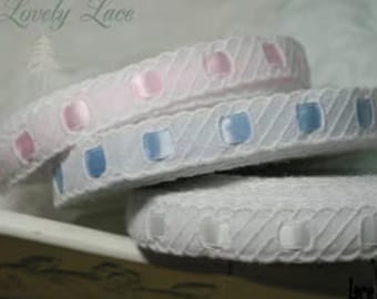 Op de afbeelding: Close-up van wit kanten lint met een geschulpte rand. Het lint is versierd met gelijkmatig verdeelde, vierkante satijnen accenten in roze, blauw en wit. De tekst "Lovely Lace" is zichtbaar in de linkerbovenhoek.