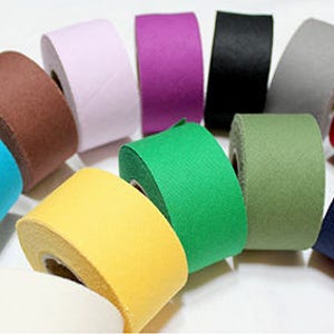May include: Assortment of 12 rolls of fabric tape in various colours, including blue, green, yellow, brown, purple, black, grey, red, and white. The tape is wound around cardboard cores.
