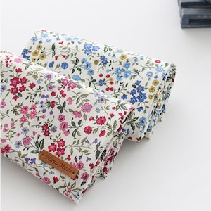 Può includere: Due rotoli di tessuto bianco con stampa floreale. Un rotolo ha una stampa floreale rosa e blu, l'altro ha una stampa floreale blu e gialla. Il tessuto è etichettato "Hand Made".
