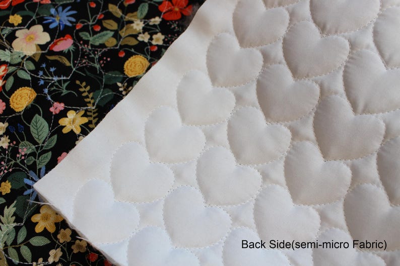 Pu&ograve; includere: Un pezzo di tessuto con un lato bianco caratterizzato da un motivo a cuori trapuntati e un lato nero con una stampa floreale colorata con fiori rossi, gialli e blu. Il testo Back Side(semi-micro Fabric) &egrave; stampato nell'angolo in basso a destra.