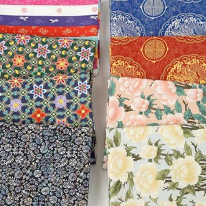Peut inclure: Une collection d'échantillons de tissu pliés présentant des motifs variés, notamment des grilles florales géométriques, des motifs de dragons traditionnels avec des emblèmes circulaires et des imprimés botaniques de fleurs.