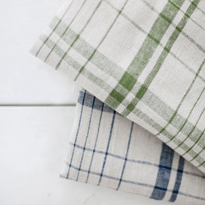 May include: Two linen tea towels with a checkered pattern. One towel is white with green checks, and the other is white with blue checks.