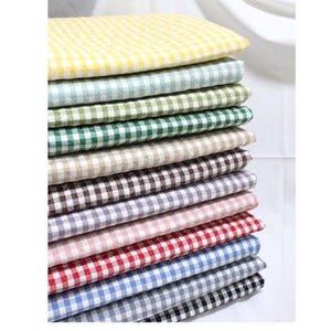 Op de afbeelding: Een stapel gewatteerde stoffen in verschillende kleuren, elk met een klassiek ruitpatroon. Kleuren zijn geel, mintgroen, bosgroen, beige, bruin, lavendel, roze, rood, blauw en zwart. De stof lijkt zacht en is waarschijnlijk geschikt voor woondecoratie of knutselprojecten.