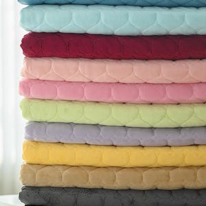 以下が含まれることがあります： ターコイズ、バーガンディ、ピンク、イエロー、グレーなど、さまざまな色の、柔らかくキルティングされた毛布の山。 各毛布はハート型の模様とビロードのような質感で、居心地の良い外観を作り出しています。