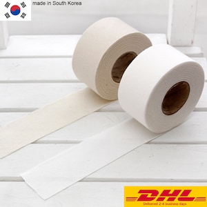 Peut inclure: Deux rouleaux de ruban adhésif en papier avec des noyaux en carton brun. Un rouleau est de couleur crème blanc cassé et l'autre est blanc vif. Les rouleaux sont placés côte à côte, chacun avec une bande de ruban s'étendant vers l'extérieur.