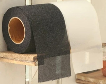 May include: A roll of black, textured tape with a wooden core sits on a small wooden shelf. A section of white, translucent tape is partially unrolled next to the black tape. The background is a white, vertical-slat wall.
