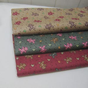May include: Three fabric swatches with gingerbread men and heart patterns. The top swatch is tan, the middle is green, and the bottom is red. The gingerbread men are brown and pink, with green and yellow hearts.