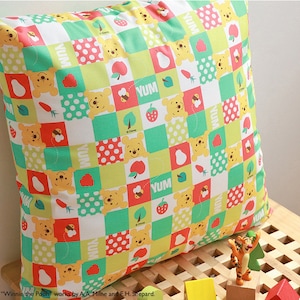 Peut inclure: Un coussin carré avec un motif patchwork représentant Winnie l'ourson et divers fruits et légumes. Le coussin est fait d'un tissu doux et blanc avec un schéma de couleurs vert, rouge et jaune. Le texte "YUM" est répété dans tout le motif.