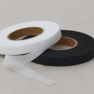May include: Two rolls of elastic tape, one white and one black, are displayed. The white tape is partially unrolled, revealing its ribbed texture. Both rolls have a wooden core. The black tape has a speckled appearance.