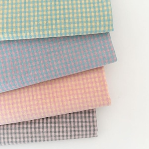 Peut inclure: Quatre échantillons de tissu pliés dans des couleurs pastel : bleu clair, rose et gris. Chaque échantillon présente un petit motif à carreaux. Les tissus sont empilés, révélant les bords et les textures du matériau.