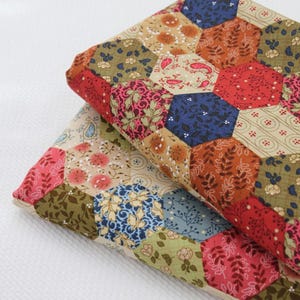 May include: A folded fabric featuring a patchwork design of hexagonal shapes. The fabric displays a variety of patterns including floral, paisley, and leaf motifs in a color palette of red, orange, blue, green, and cream, arranged in a repeating geometric grid.
