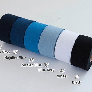 May include: A cylindrical roll of fabric tape featuring six distinct colour segments labelled with numbers and names: 36 Deep Navy, 37 Majolica Blue, 38 Persian Blue, 39 Blue Gray, 40 White, and 41 Black. The tape has a smooth, matte texture and is arranged horizontally.