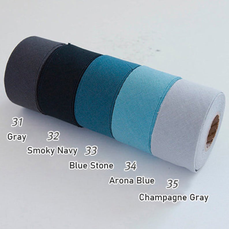 May include: A cylindrical roll of fabric tape featuring five distinct colour segments labelled with numbers and names: 31 Gray, 32 Smoky Navy, 33 Blue Stone, 34 Arona Blue, and 35 Champagne Gray. The textile material has a visible woven texture.