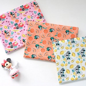 Peut inclure: Trois échantillons de tissu avec un fond rose, orange et blanc. Chaque échantillon présente un motif répétitif de Mickey Mouse avec des fruits, notamment des citrons, des oranges et des pastèques.