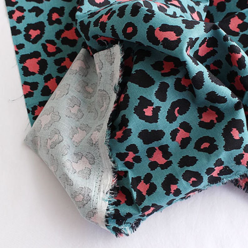 May include: Teal fabric with a pink and black leopard print pattern. The fabric is folded and the edges are frayed.