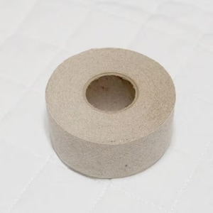 May include: A roll of tan-colored tape with a central hole. The tape appears to be made of a fibrous material, and the roll is sitting on a white, quilted surface. The tape is circular in shape.